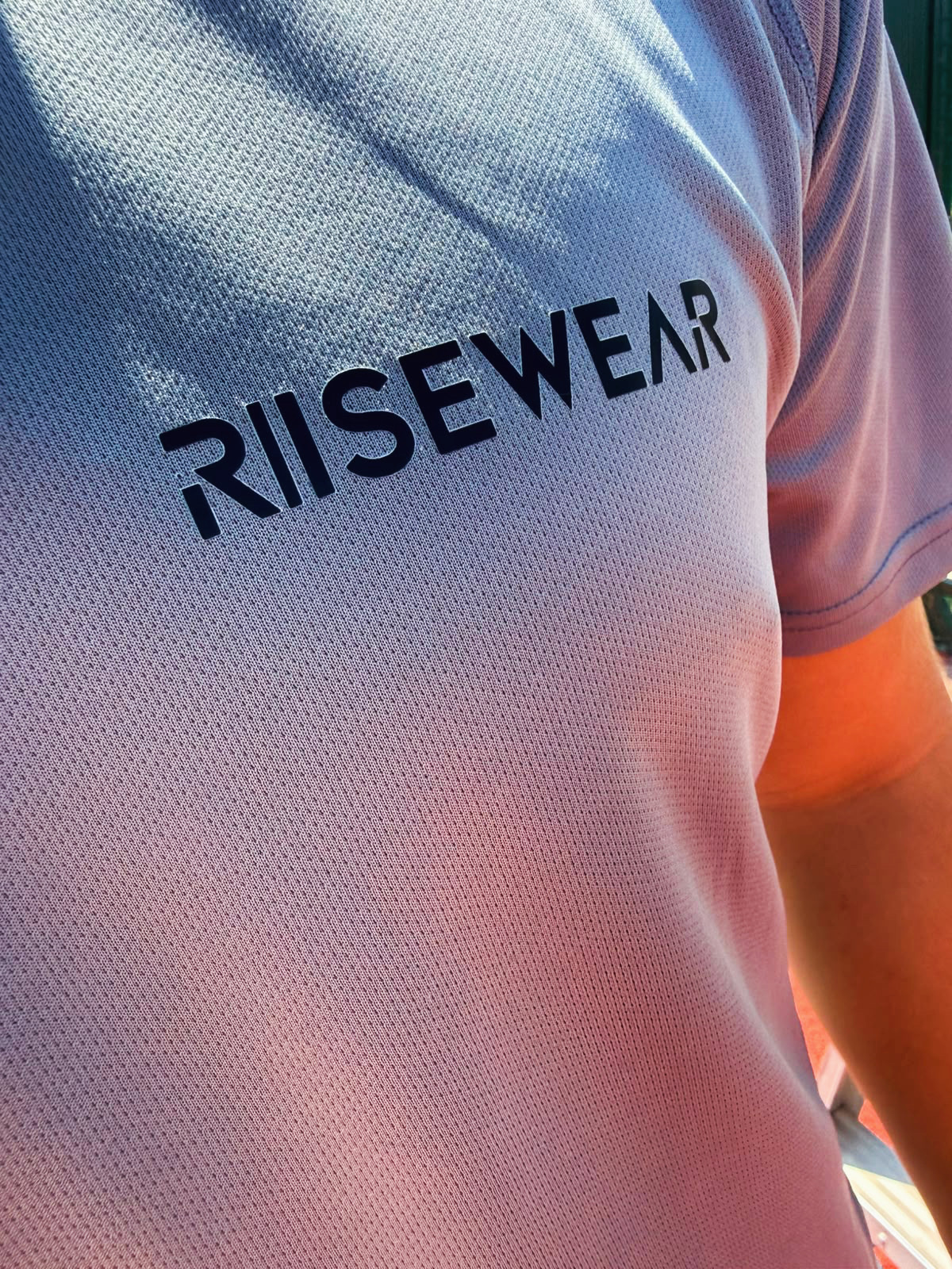 Close-up van het Risewear logo op een grijs shirt